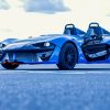Zenos E10 de couleur bleue vue de 3/4 avant statique dans les stands d'un circuit automobile.